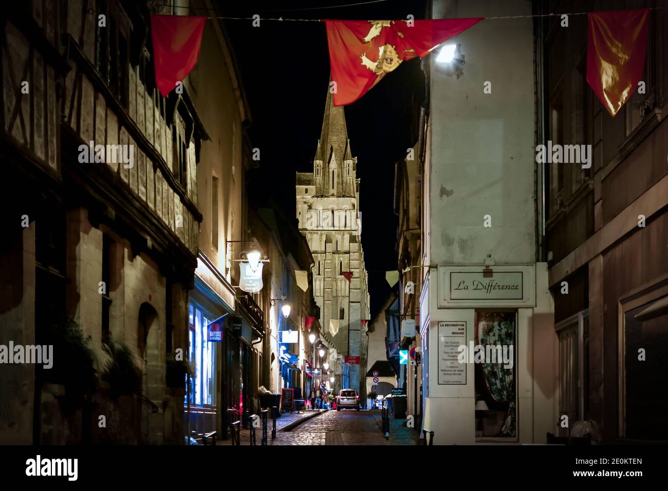 Vista notturna della zona medievale della città vecchia di Bayeux, Francia, con la Cattedrale di Bayeux in vista e la bandiera del Calvados appeso di fronte alla strada. Foto Stock