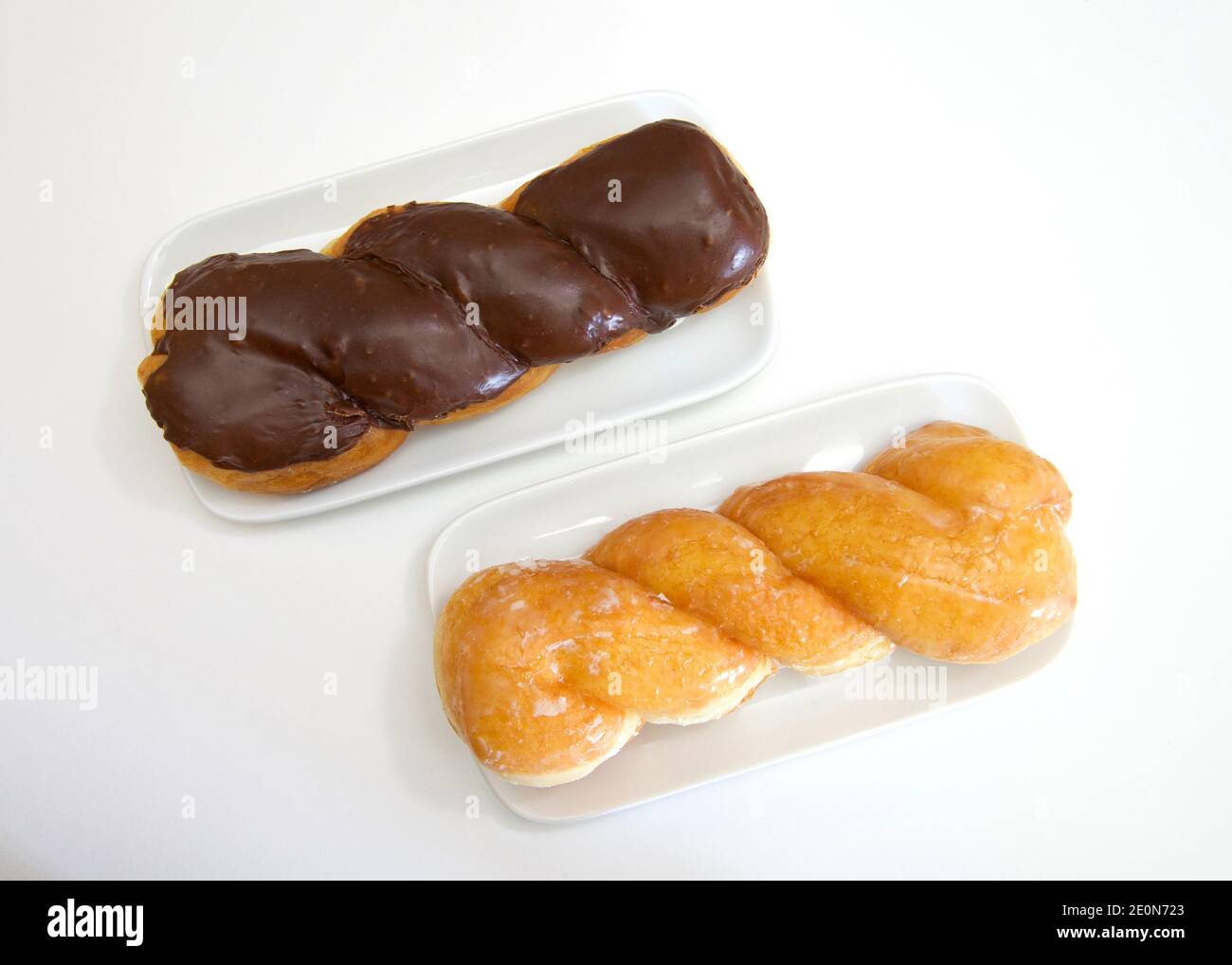 Vista dall'alto piatto di una ciambella ritorcitura smaltata e una torsione smaltata ricoperta di cioccolato su piastre rettangolari in porcellana bianca, su carta pergamena. Foto Stock