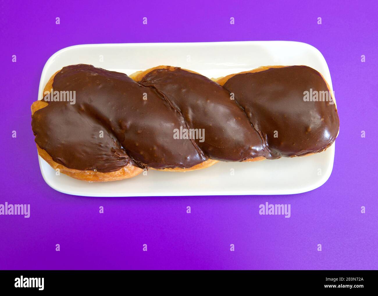 Vista dall'alto piatto di una ciambella ritorcitura smaltata su un piatto rettangolare di porcellana bianca, su sfondo viola. Foto Stock