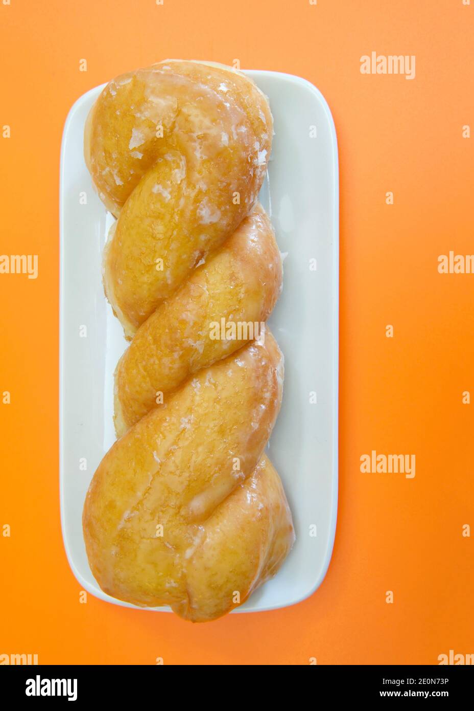 Vista dall'alto piatto di una ciambella ritorcitura smaltata su una piastra rettangolare in porcellana bianca, su sfondo arancione. Foto Stock