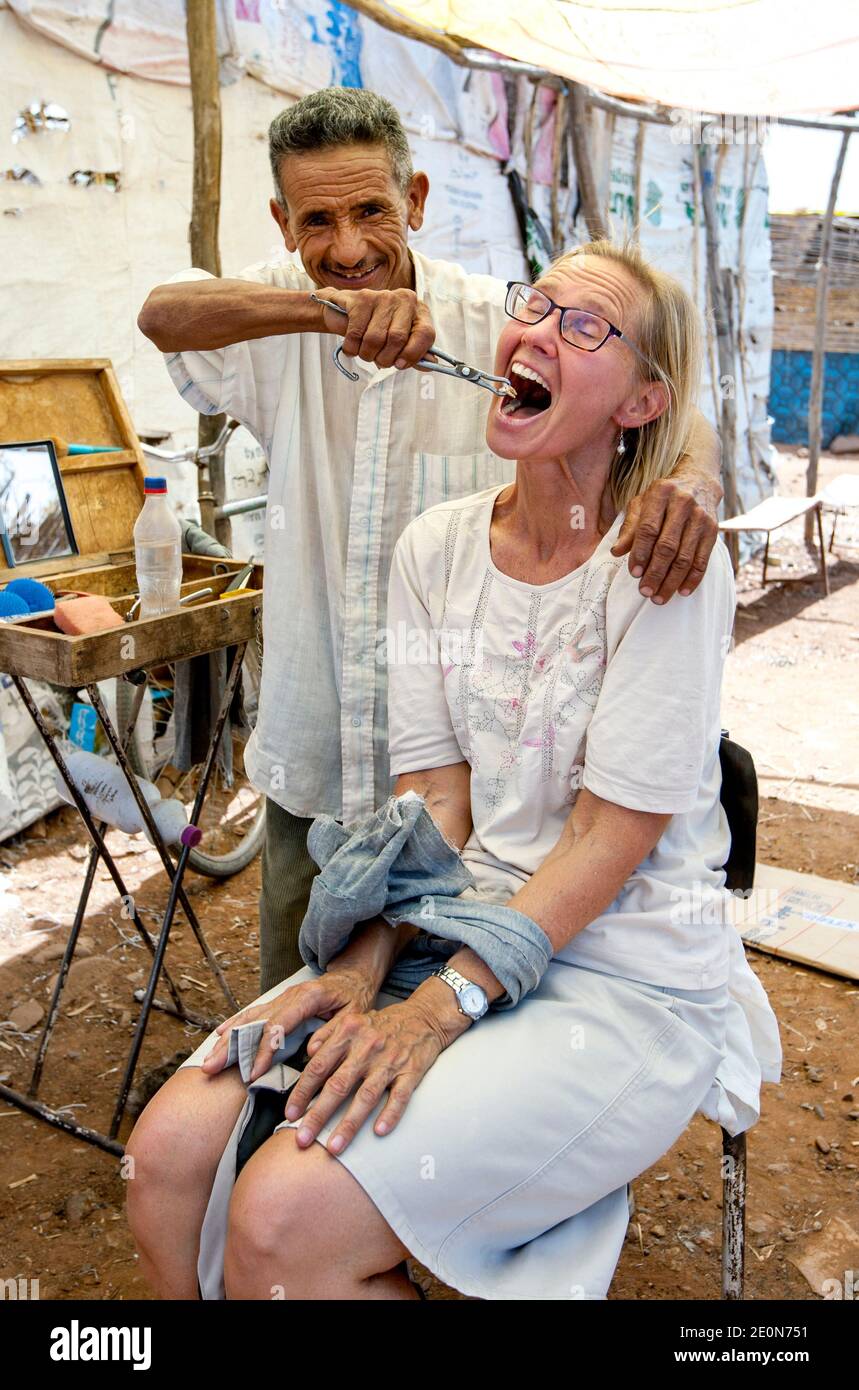 Il dentista locale al mercato di Tahanoute in Marocco finge di estrarre un dente dalla bocca di una donna straniera. Foto Stock