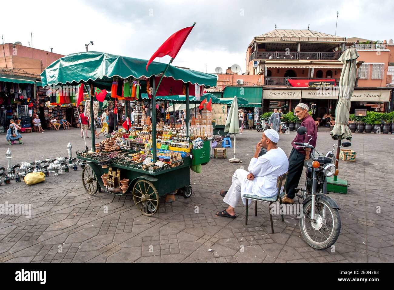 Un uomo siede accanto al suo stand portatile che vende una varietà di beni a Djemaa el-Fna, la piazza principale della medina di Marrakech in Marocco. Foto Stock