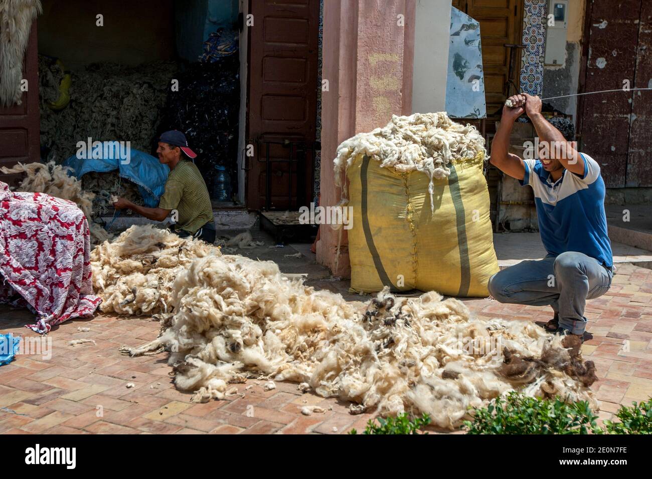 Un uomo batte un mucchio di lana con una barra di metallo per rimuovere le impurità prima che la lana sia imballata in balle ad un commercio a Meknes, Marocco. Foto Stock