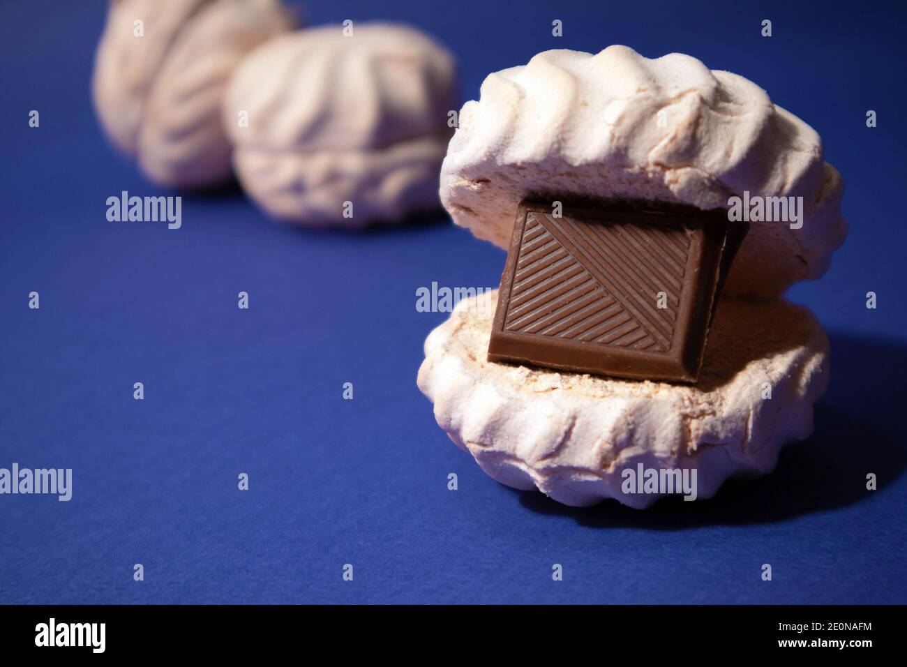 zephyr bianco con mattonella di cioccolato fondente all'interno contro trendy sfondo blu Foto Stock