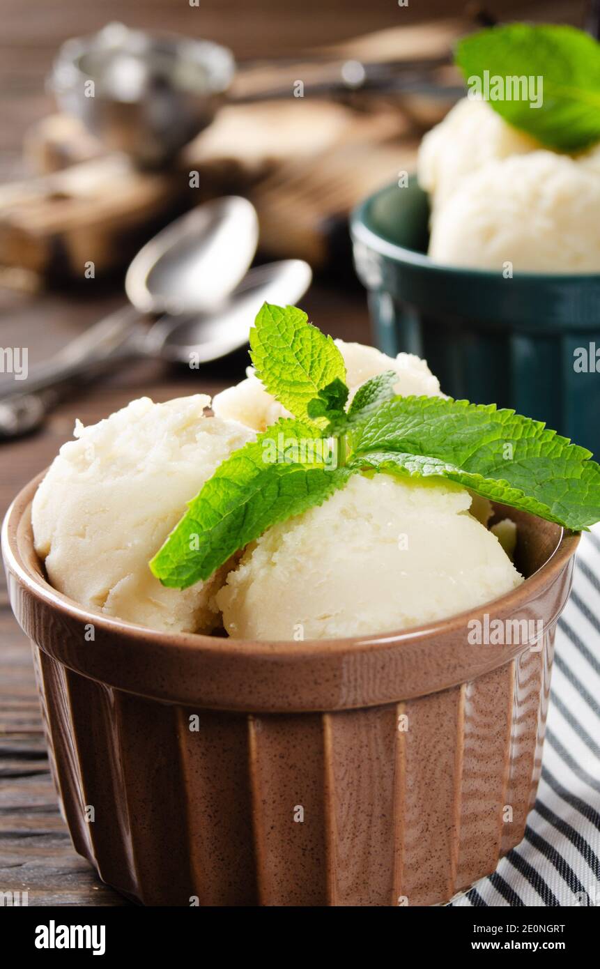 Palline di icecream alla vaniglia in ciotole di argilla su tavolo da cucina  in legno con paletta per gelato da parte Foto stock - Alamy