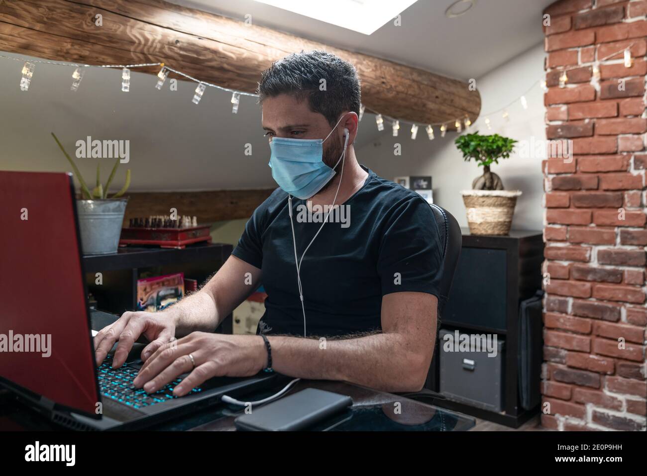 Uomo con maschera chirurgica che lavora da casa causa di confinamento per il coronavirus covid-19 Foto Stock