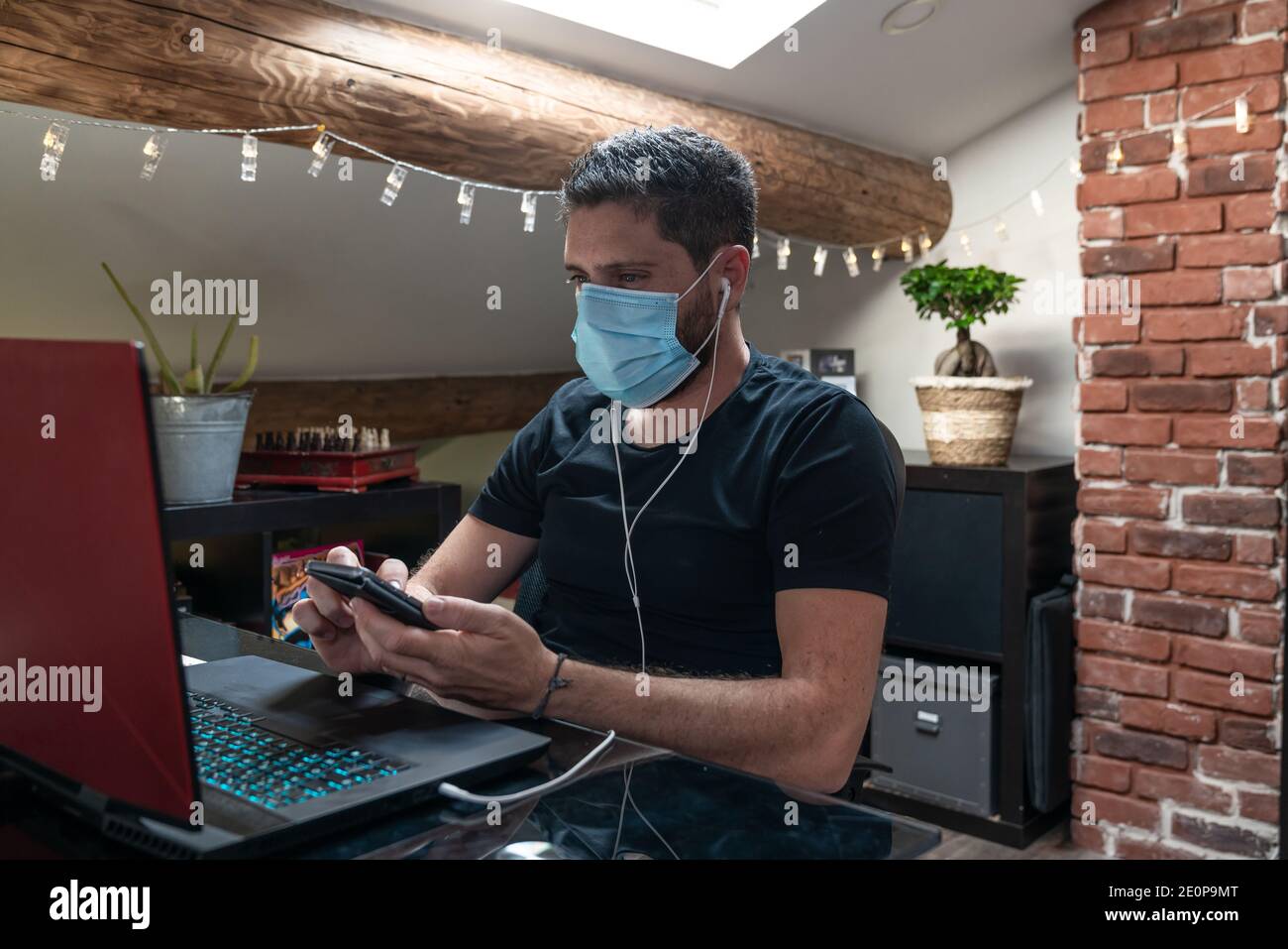 Uomo con maschera chirurgica che lavora da casa causa di confinamento per il coronavirus covid-19 Foto Stock