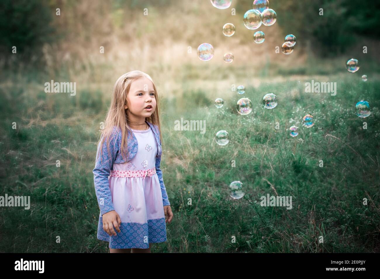 La bambina ride giocando con bolle di sapone per strada in estate. Foto Stock