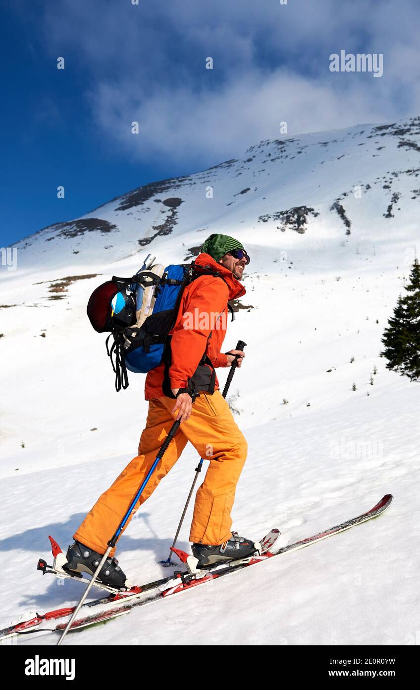 Uomo scialpinista che raggiunge la cima in montagne innevate, in giornata di sole. Neve e attività invernali, sciare in montagna. Foto Stock