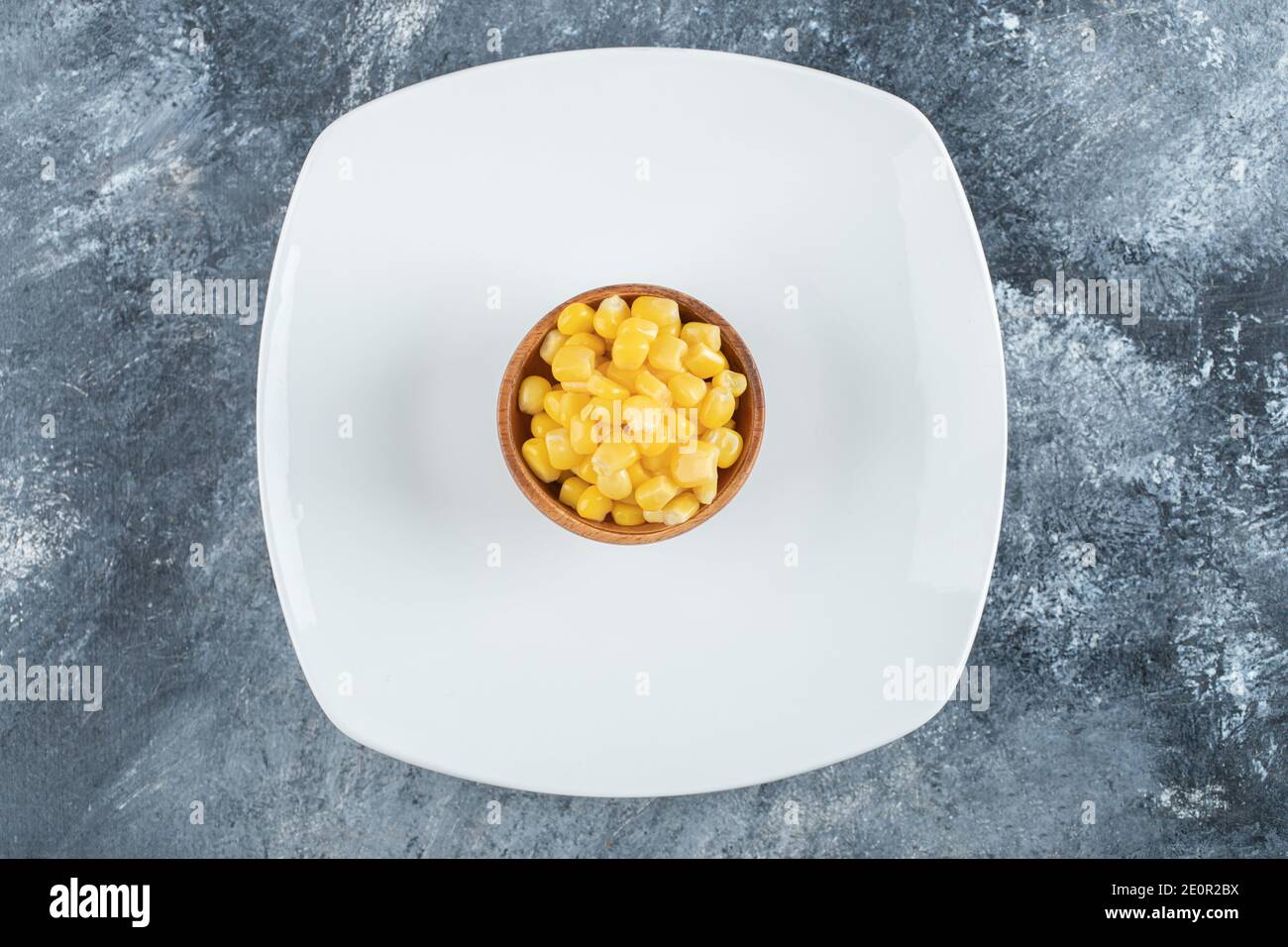 Una ciotola di legno di semi di popcorn su una piastra vuota Foto Stock