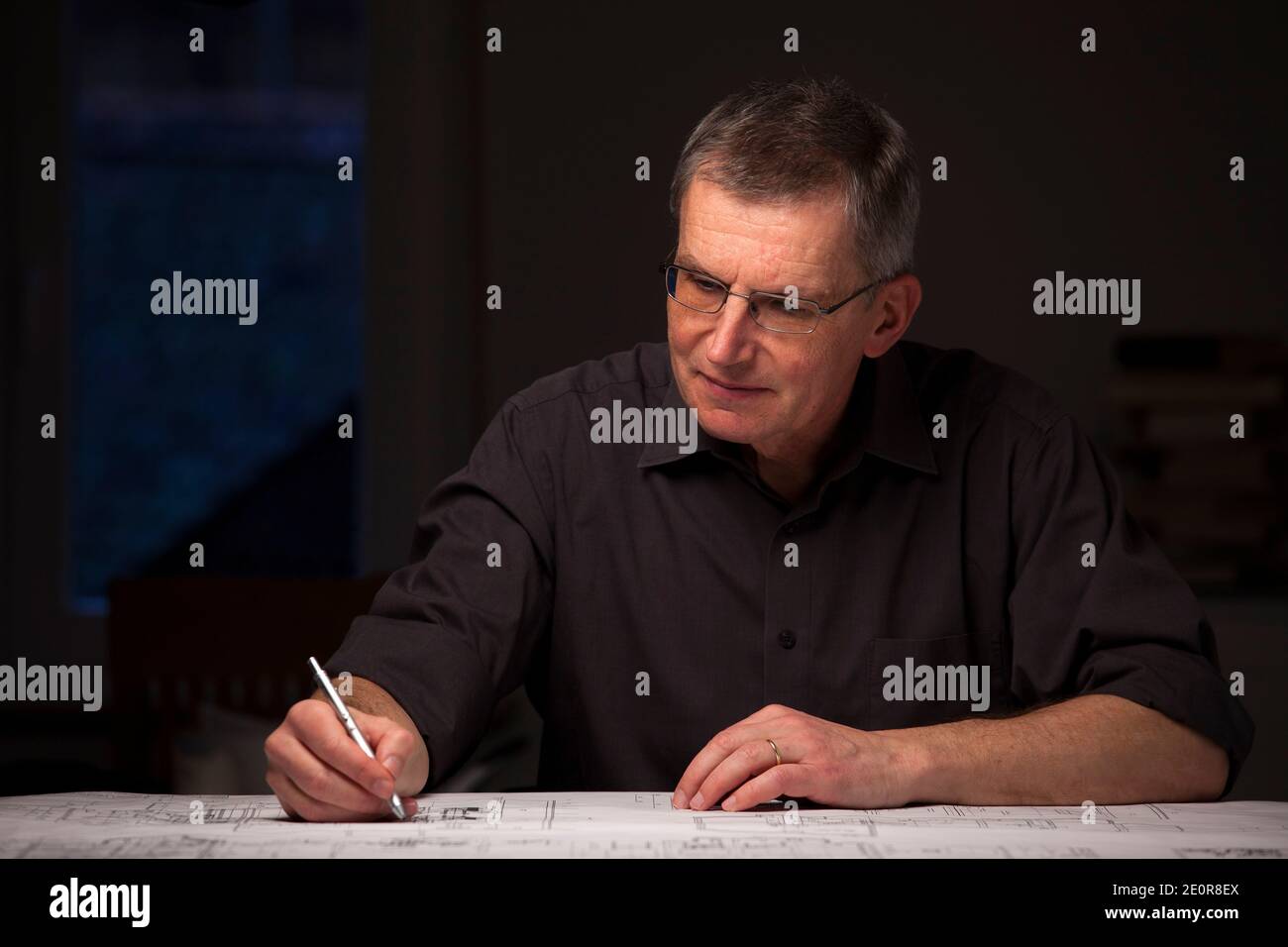 Ingegnere concentrato o architetto in camicia scura che lavora a casa di notte - mettere a fuoco sul viso Foto Stock