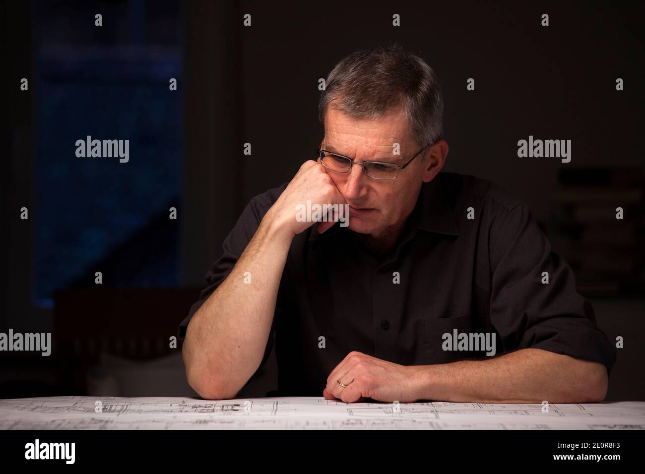 Ingegnere pensivo o architetto in camicia scura guardando il blueprint a casa di notte - mettere a fuoco sul viso Foto Stock