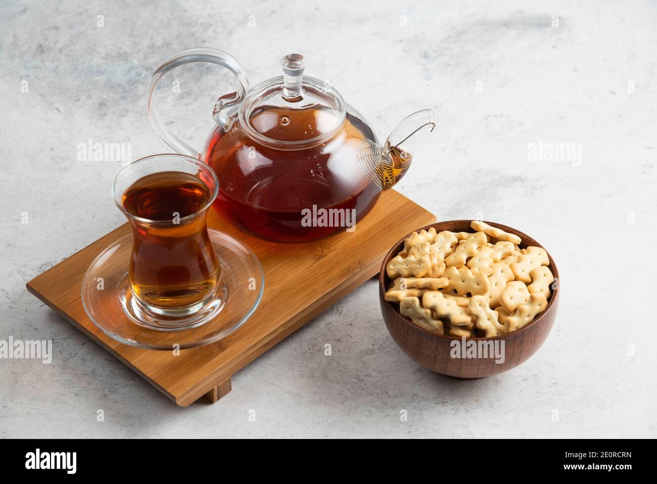 Una tazza di tè di vetro con ciotola di legno piena di cracker Foto Stock