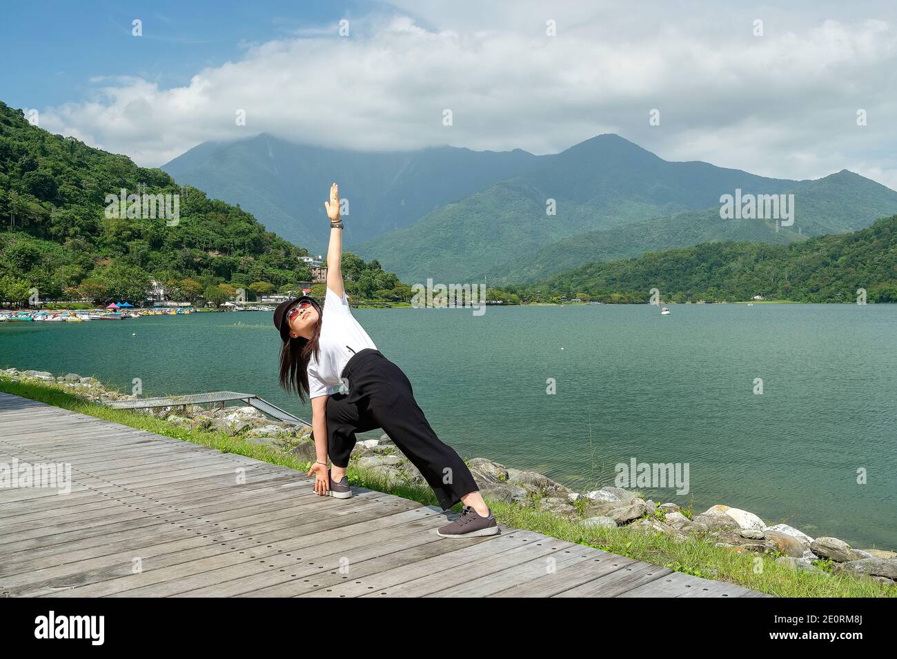 Donna asiatica in abiti casual che tiene una posa yoga su una passerella sul lago con la vista del lago e delle montagne sul lago di Carp sullo sfondo, Taiwan Foto Stock