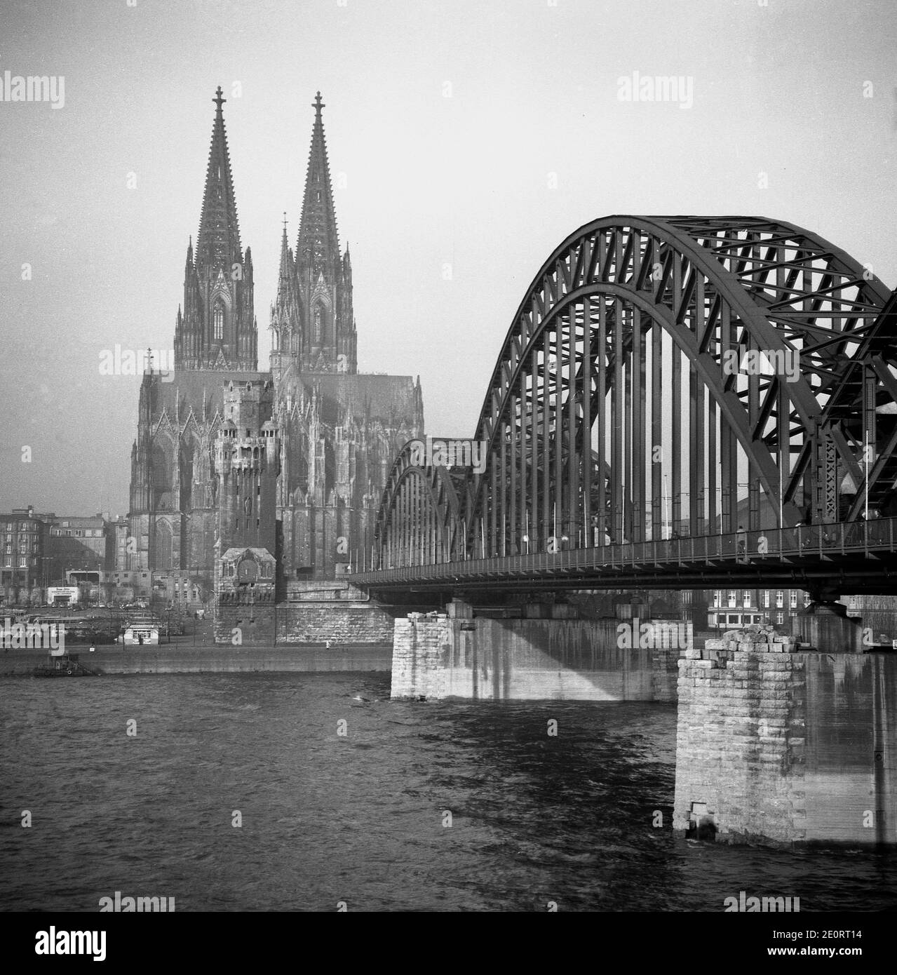 1950, storico, vista del dopoguerra dall'altra parte del fiume Reno del Ponte Hohenzollern - in questo momento solo un ponte ferroviario e pedonale - e la Cattedrale cattolica di Koln a due punte che sopravvisse ai bombardamenti degli Alleati del WW2. La costruzione di questo famoso monumento tedesco iniziò nel 1248, ma la chiesa in stile gotico non fu completata fino a molto più tardi nel 1880. Foto Stock