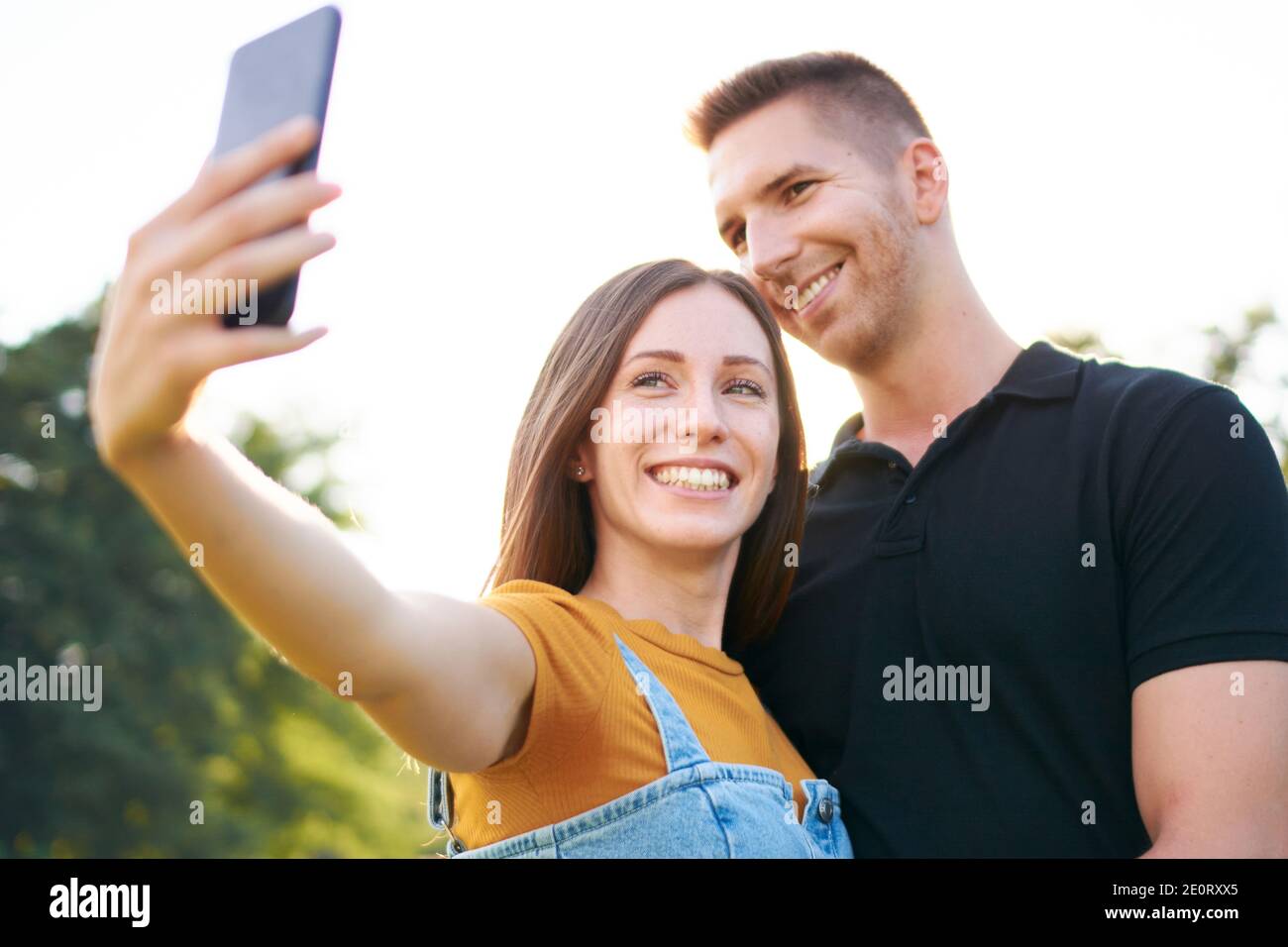 Giovane felice millennial coppia sorridente e prendendo selfie - Z Generazione di turisti che si divertono insieme - concetto di tecnologia con un smartphone e amici Foto Stock