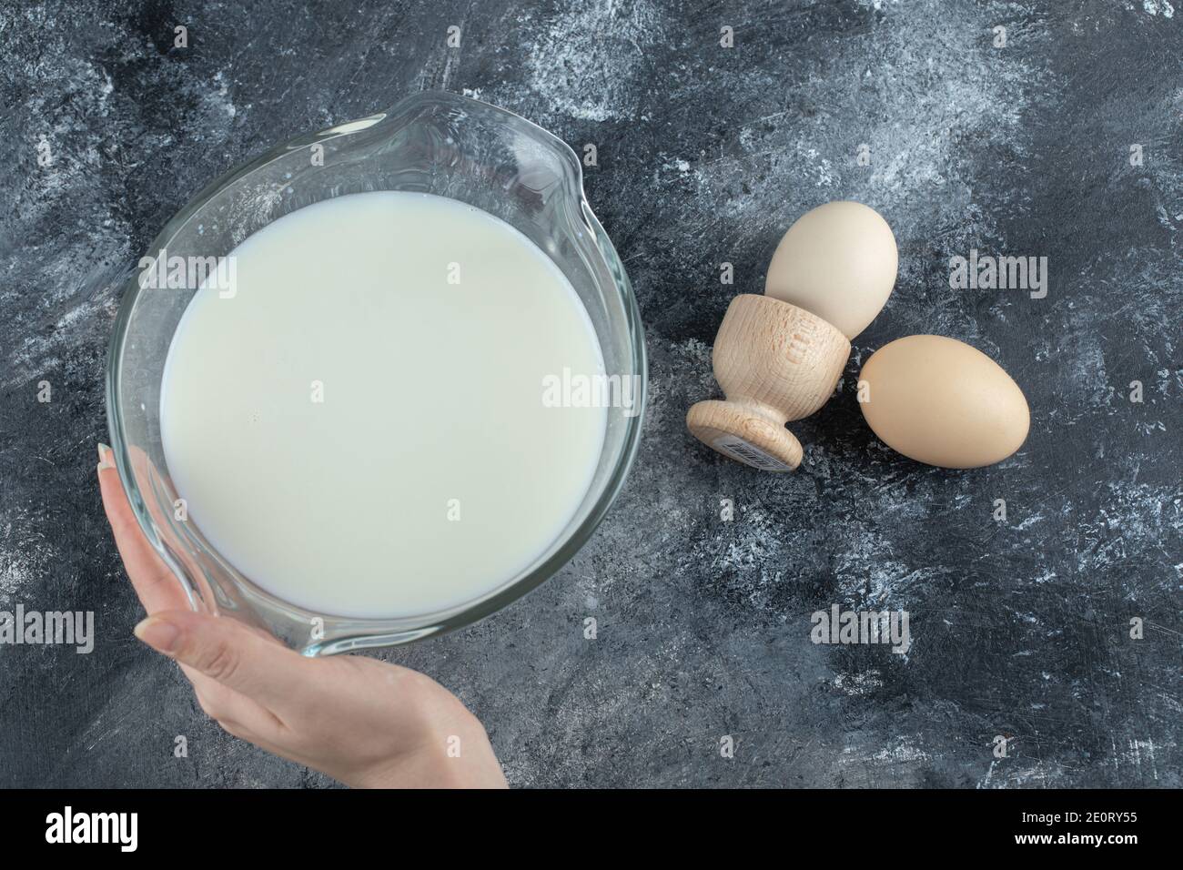 Mano femmina che tiene la ciotola di latte su fondo di marmo Foto Stock