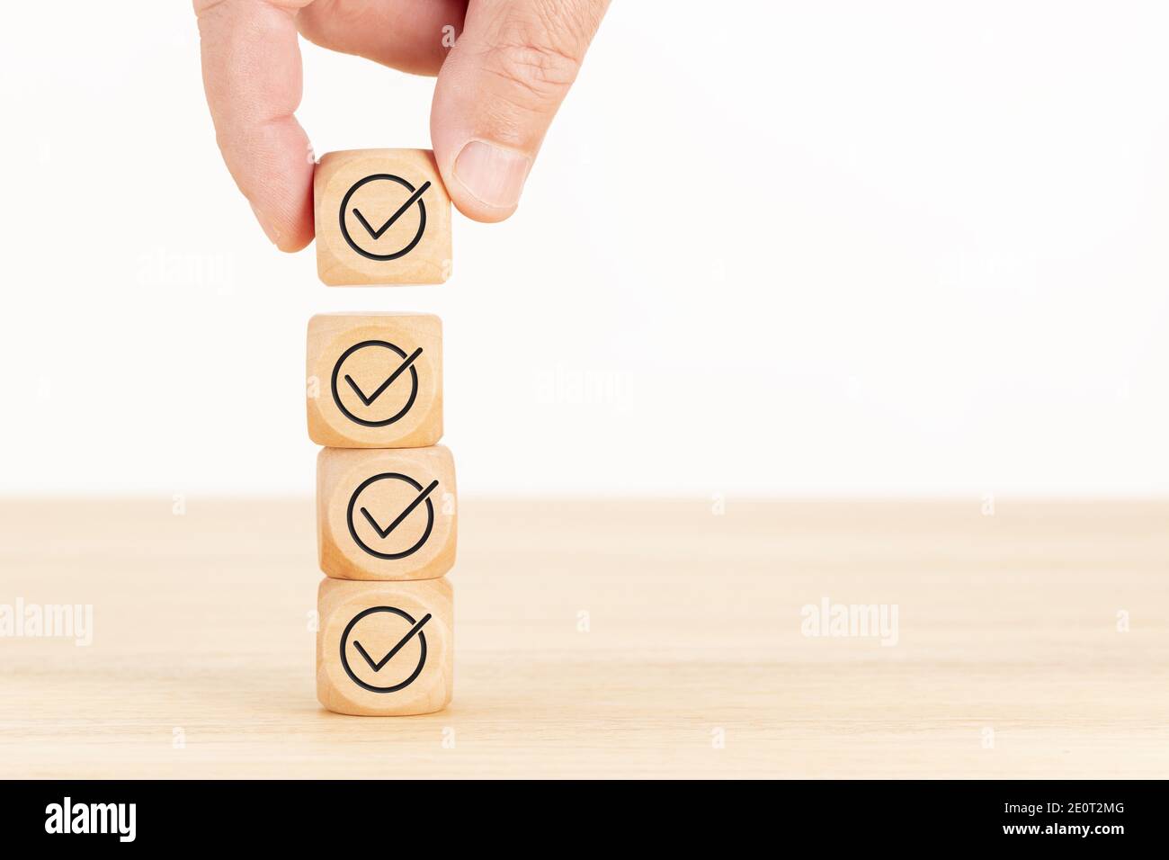 Concetto di controllo o lista di controllo. Blocco cubo di legno selezionato a mano con icona di controllo accatastata su un tavolo di legno. Spazio di copia Foto Stock