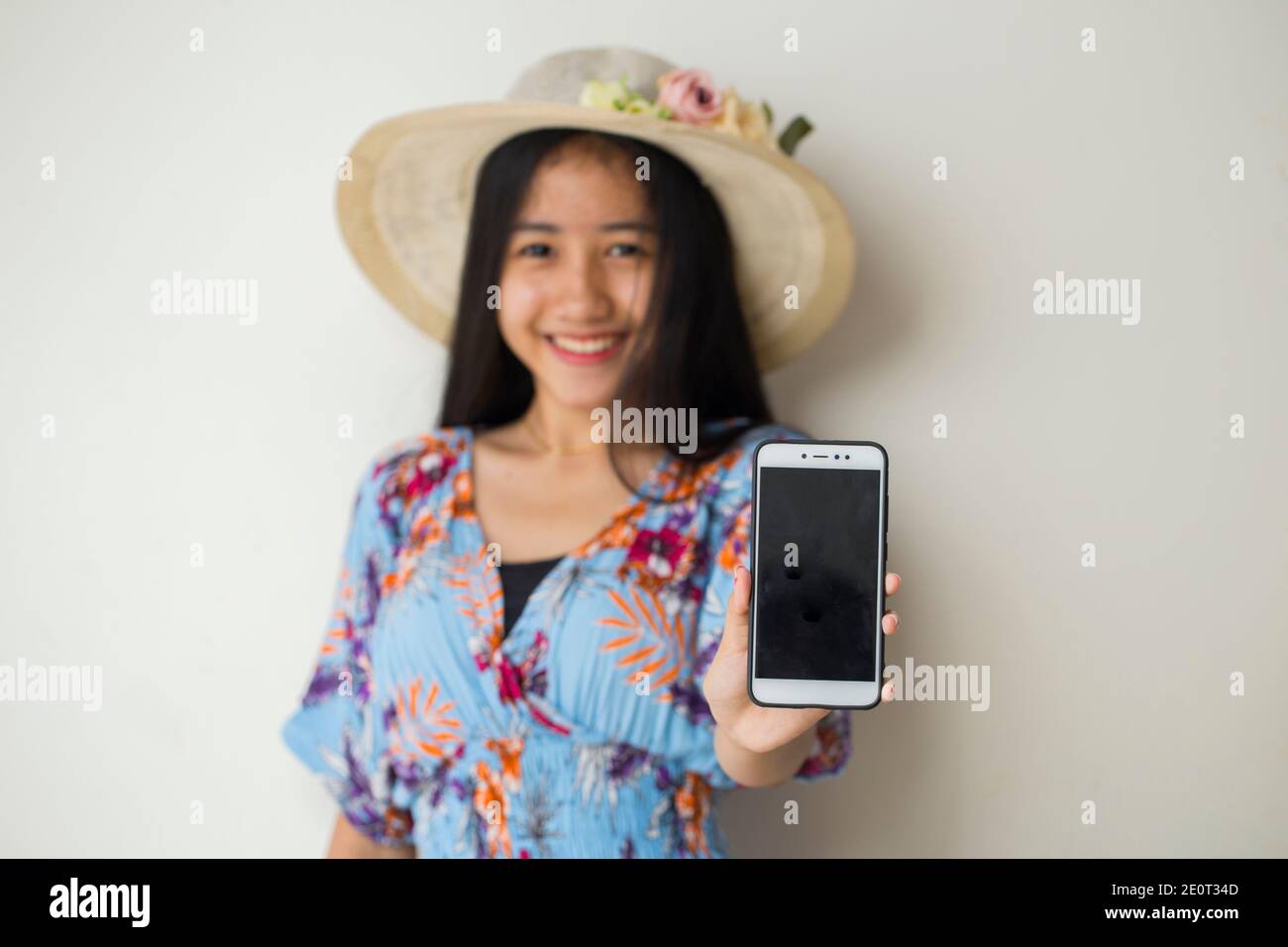 Felice viaggiatore asiatico donna dimostrare cellulare. Ritratto di ragazza sorridente, che posa su sfondo bianco Foto Stock