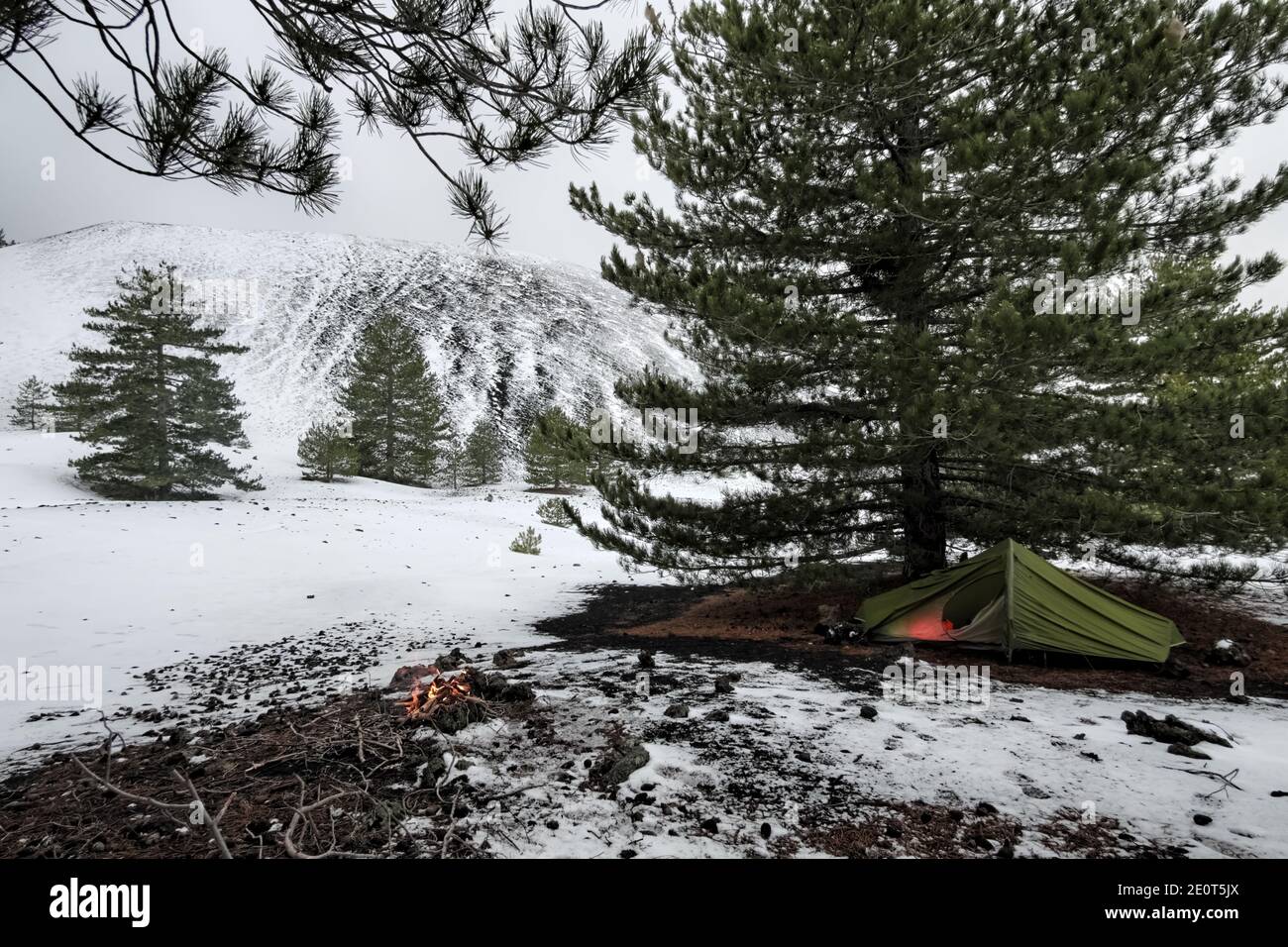 Campeggio selvaggio invernale con fuoco, tenda trekking in alberi di pino nel Parco dell'Etna, delle attività all'aperto in Sicilia un punto di riferimento Foto Stock