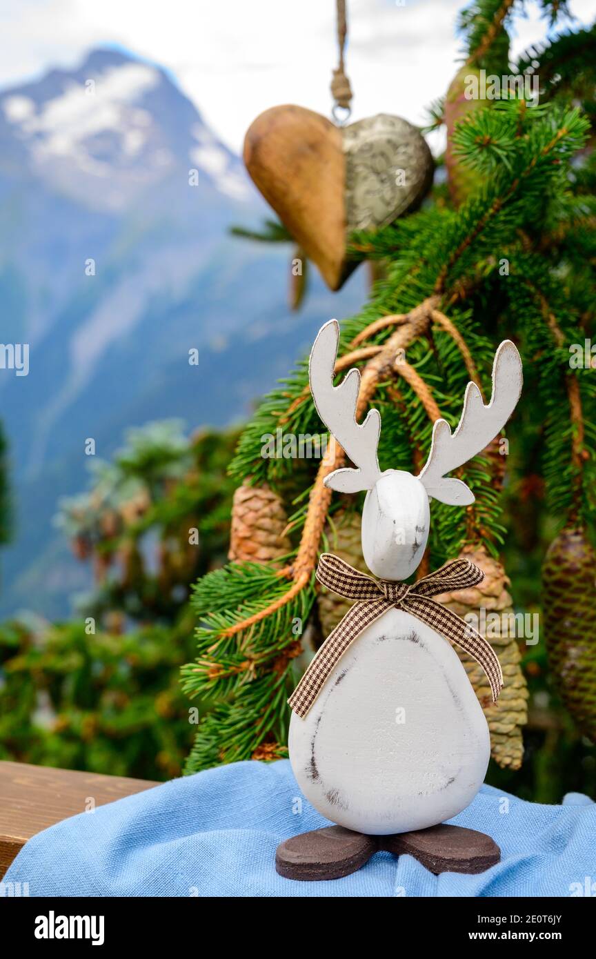 Albero di Natale verde con coni che crescono nelle Alpi francesi montagne decorato con cuore in legno sospeso e alci e montagne natalizie picchi sul backgr Foto Stock