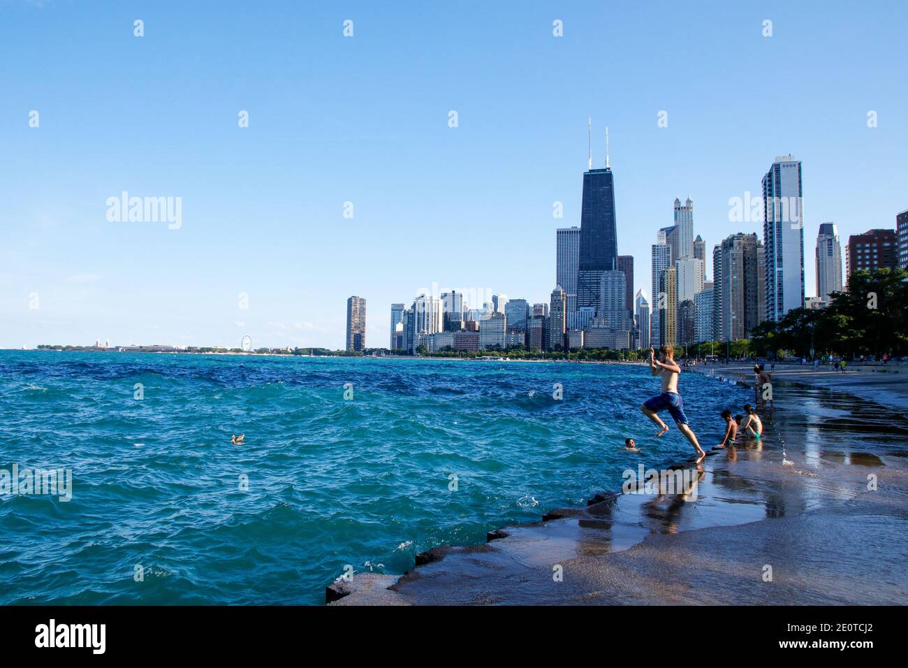 Fronte lago di Chicago vicino a North Avenue Beach. Giovane uomo che salta dal muro di mare al lago. Foto Stock