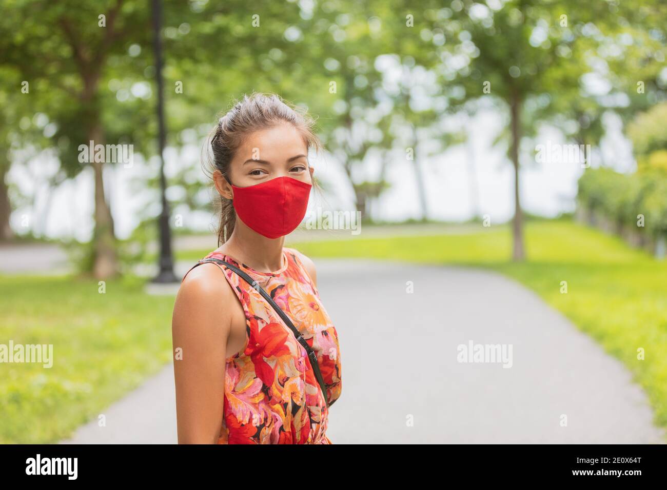 Donna asiatica che indossa la copertura facciale che cammina sulla strada mentre aspetti fuori dalla fermata dell'autobus per i trasporti pubblici. Ritratto estivo di moda in maschera rossa Foto Stock