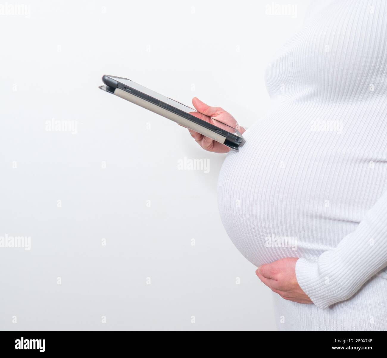 Contenuto donna incinta che tiene la sua tavoletta stanting in vita camera a casa Foto Stock