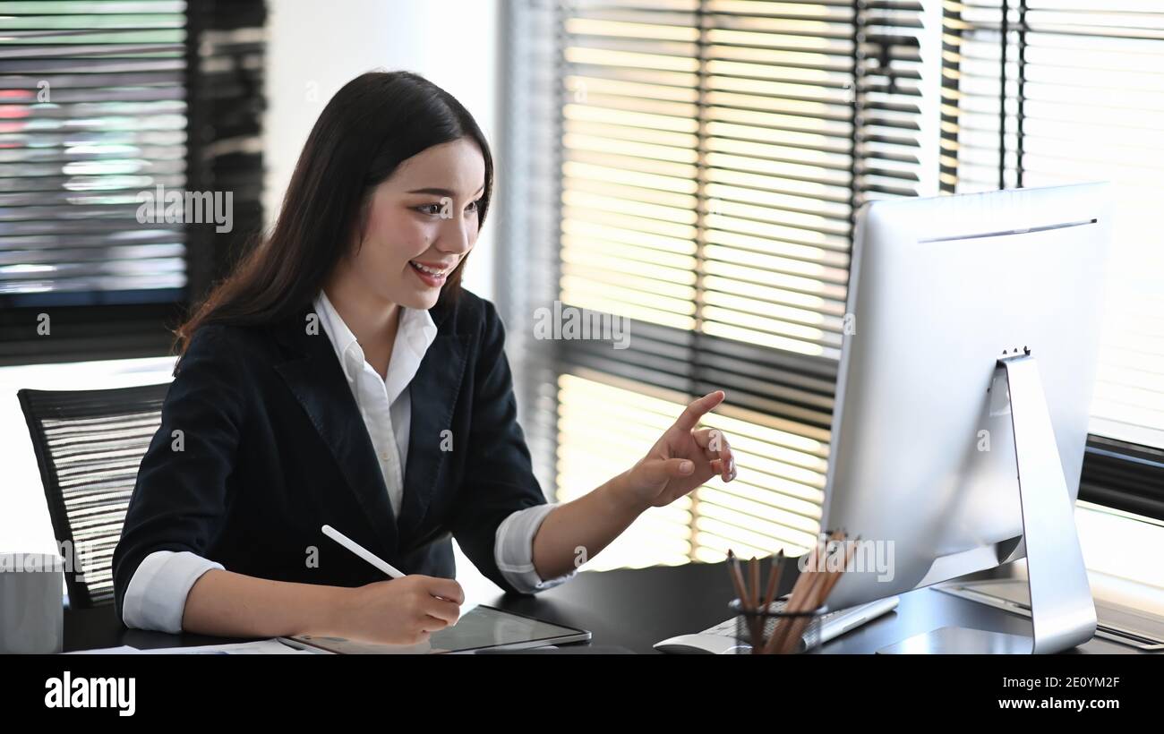 Una bella giovane donna in tuta mano facendo nota e puntando allo schermo del computer. Foto Stock