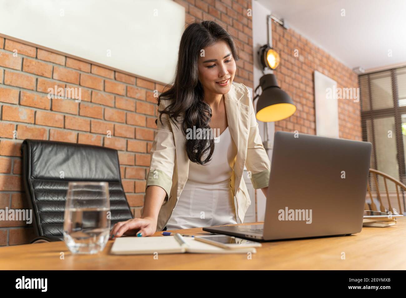 Giovane bella donna d'affari asiatica che guarda il suo computer sul tavolo del suo salotto a casa sua, concetto di lavoro a casa Foto Stock