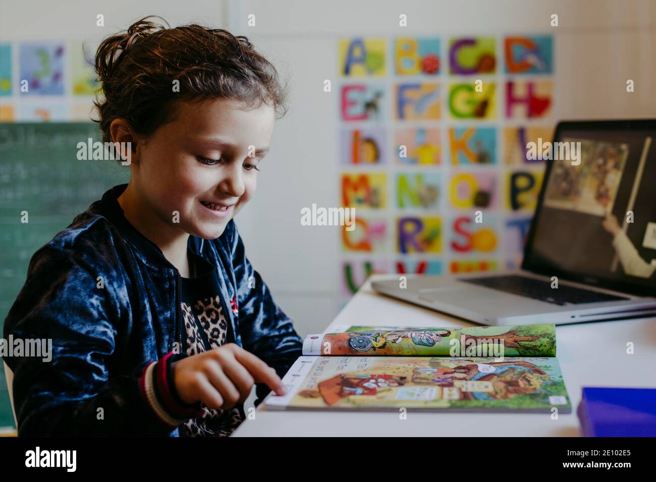 Bambina che impara con il libro di lettura e il laptop, homeschooling Foto Stock