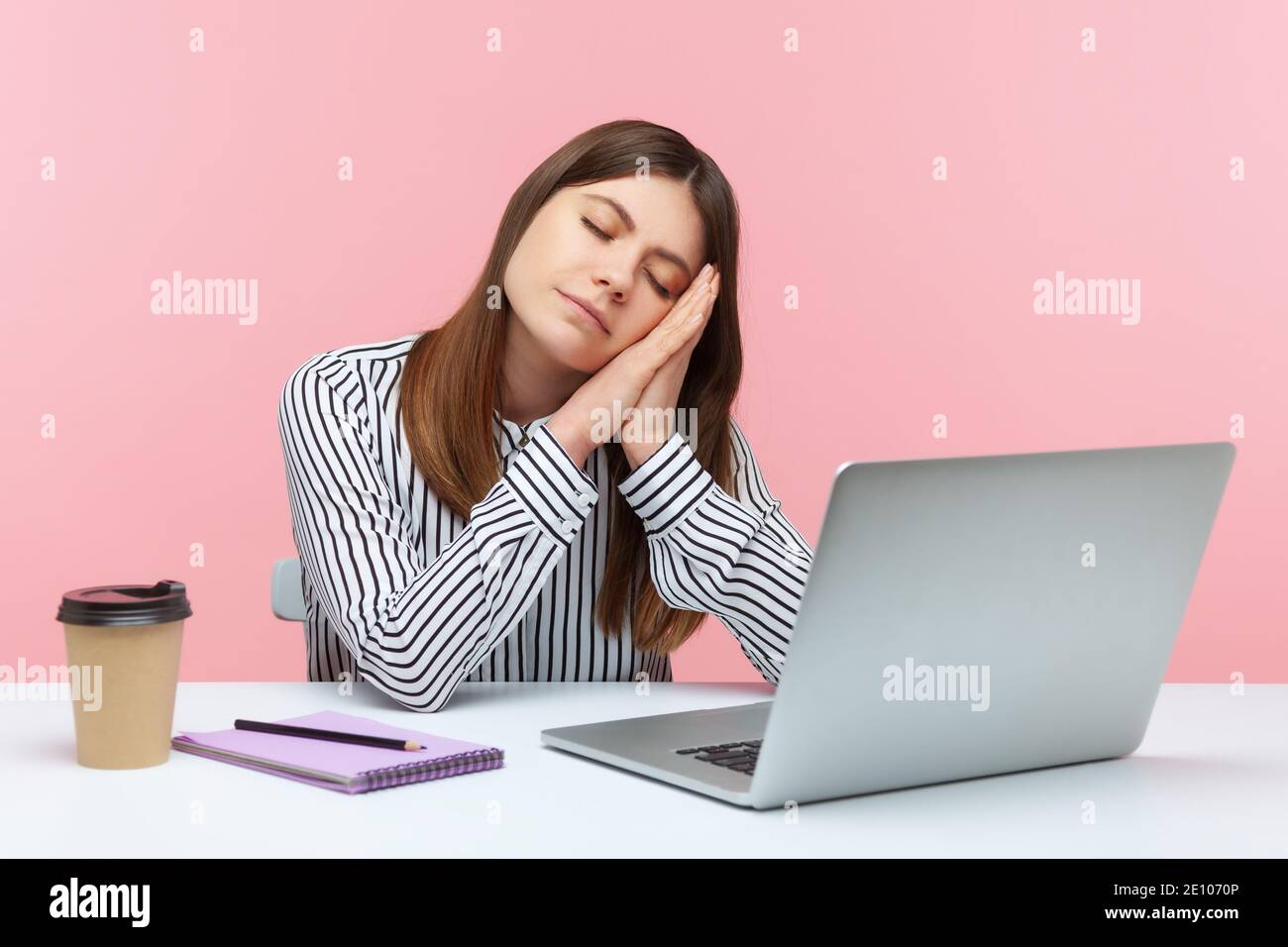 Annoiata lavoratrice d'ufficio addormentata in camicia a righe che pende la testa appoggiandosi sulle mani seduto sul posto di lavoro con un computer portatile, lavoro eccessivo, risveglio precoce. Interno Foto Stock