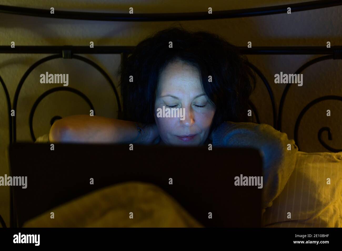 Donna stanca che lavorava su un computer portatile di notte si è coccolata nel suo letto sfregando la parte posteriore del suo collo a. alleviare la tensione nei muscoli Foto Stock