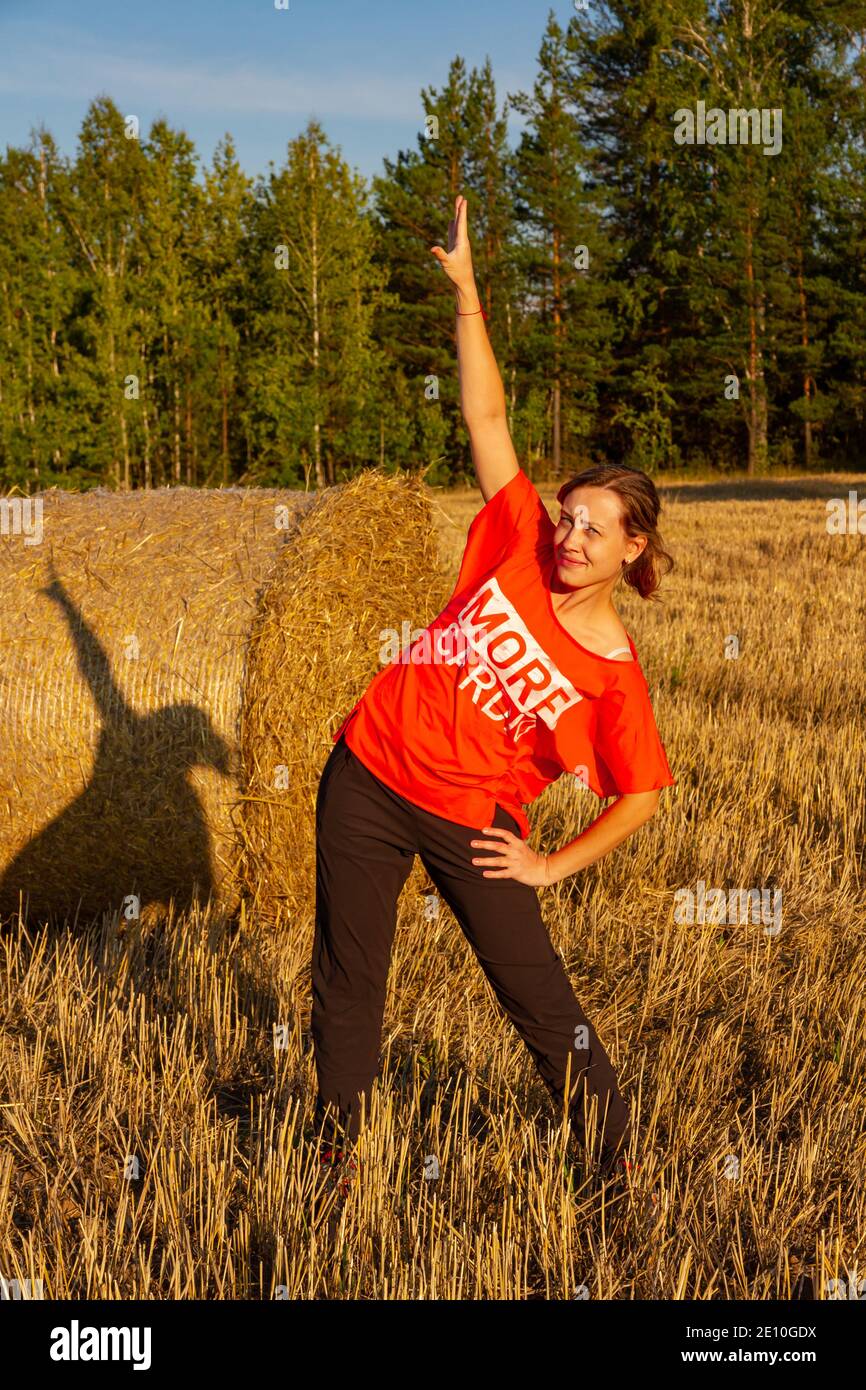 giovane bella ragazza in uniforme sportiva facendo ginnastica all'aperto in il campo dal haystack Foto Stock