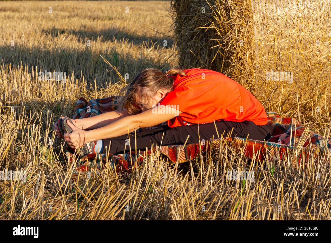 una giovane bella ragazza in una divisa sportiva è impegnata in yoga all'aperto in un campo sullo sfondo di uno stack di fiati al tramonto Foto Stock