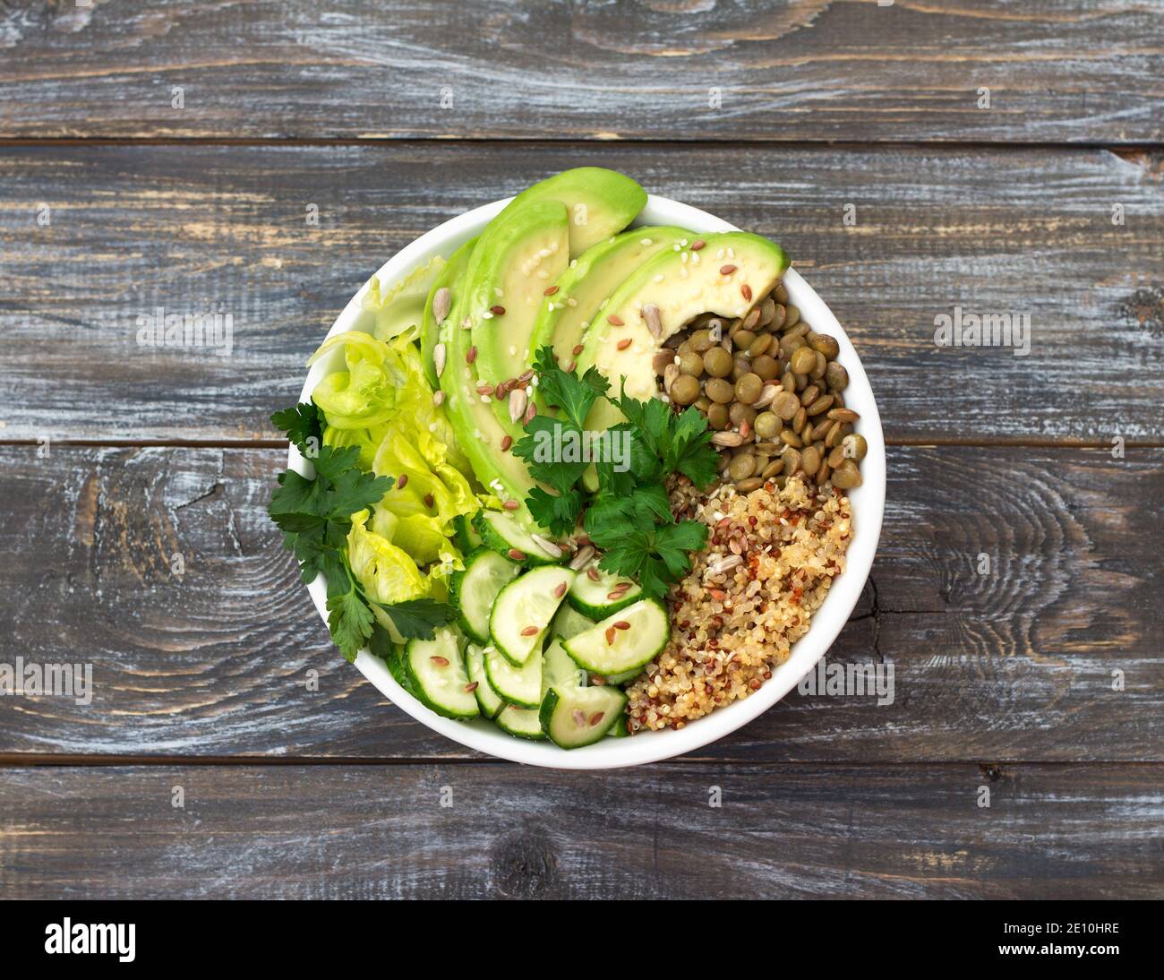 Coppa di Buddha verde con lenticchie, quinoa, avocado, cetriolo, lattuga fresca, erbe e semi. Cibo sano e salutare. Su sfondo di legno, Foto Stock