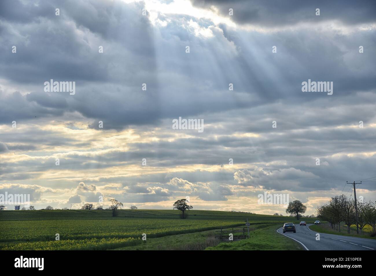 Auto singola su una lunga strada in lontananza la campagna sotto un cielo nuvoloso con raggi di sole sulla strada che ci attende Foto Stock