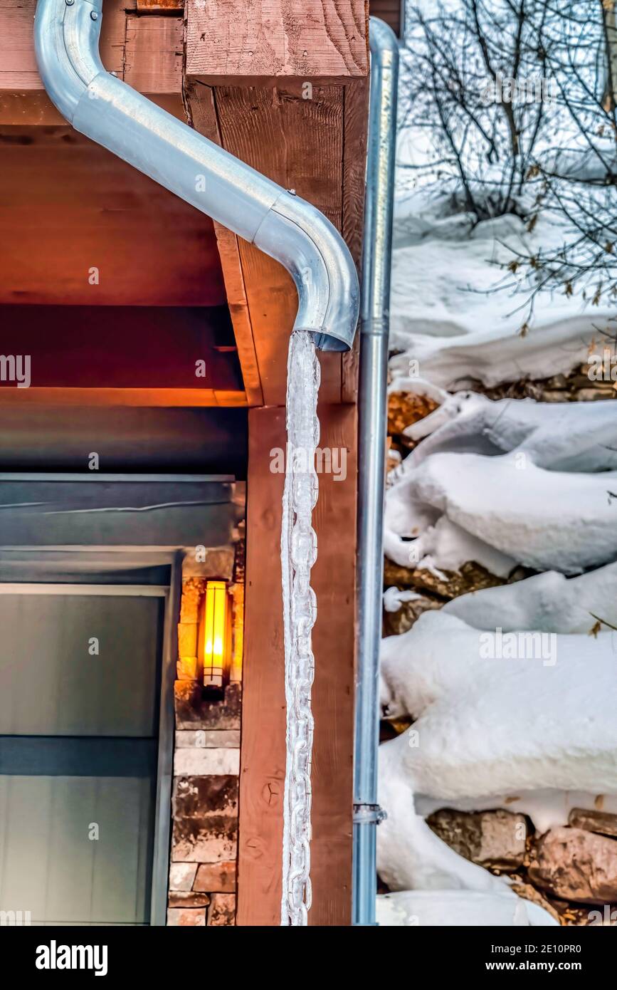 Tubo di scarico del tetto di casa con acqua surgelata contro neve e pendio  roccioso della collina Foto stock - Alamy