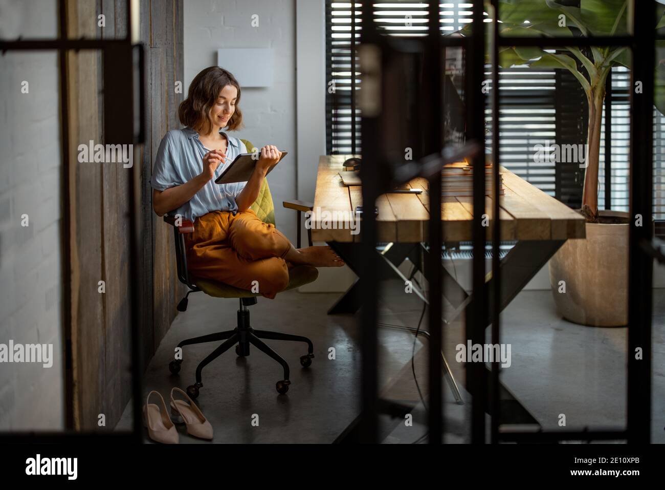 Donna creativa che lavora su un touchpad nell'accogliente ed elegante ufficio domestico. Scatto completo Foto Stock