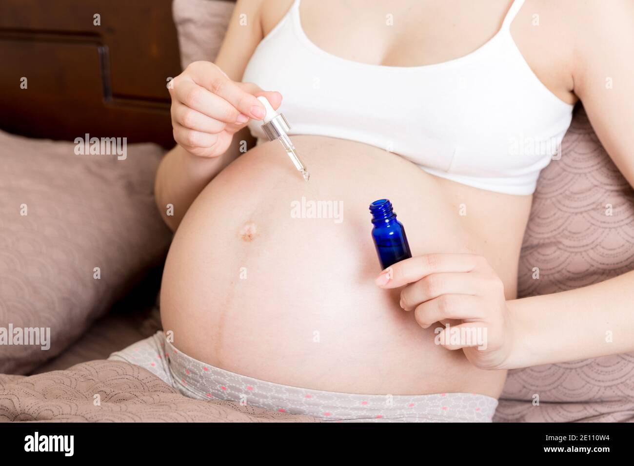 una ragazza incinta si siede a casa sul letto e gli strisci sorridono una crema di marcatura anti-stretch sul suo stomaco. Gravidanza, maternità, preparazione e attesa Foto Stock