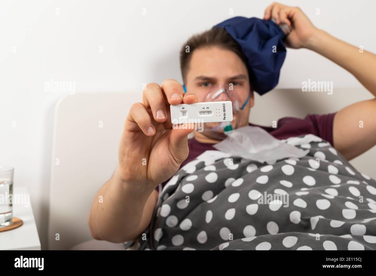 Covid-19 paziente di sesso maschile che si trova a letto a casa sta tenendo un test rapido della covide dell'antigene Foto Stock