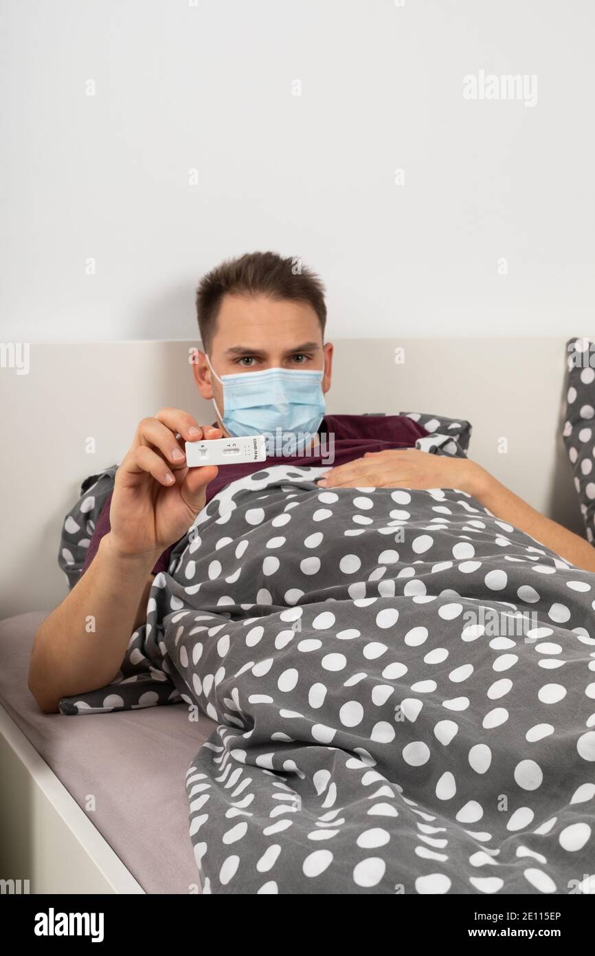 Covid-19 paziente di sesso maschile che si trova a letto a casa sta tenendo un test rapido della covide dell'antigene Foto Stock
