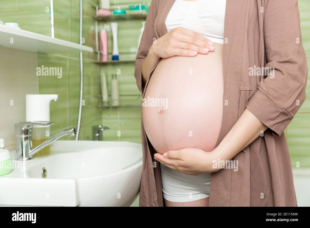 Giovane donna incinta vestita in un accappatoio nella toilette di casa.  Carino ragazza adulta nel terzo trimestre di gravidanza in un bagno di  casa. Gravidanza, madre Foto stock - Alamy