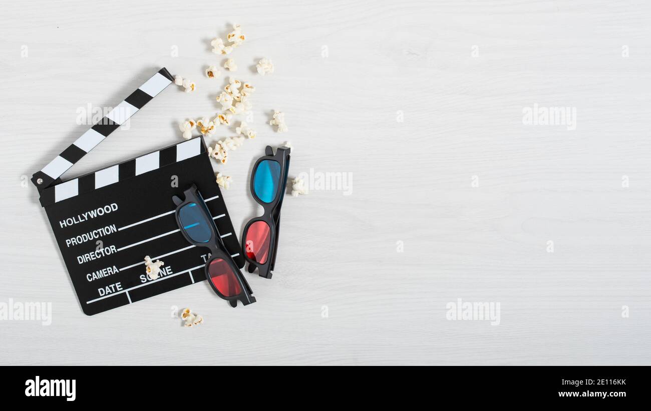 Clapperboard cinematografico, colorati occhiali 3d e popcorn su sfondo bianco legno vista dall'alto. Sfondo cinematografico. Foto Stock