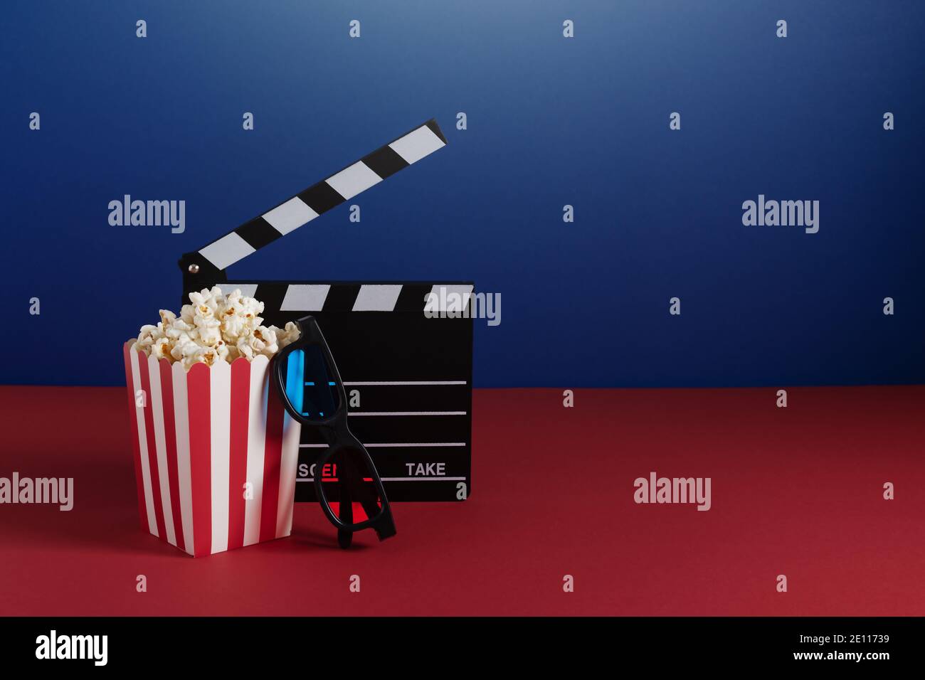 Clapperboard per cinema, occhiali 3d colorati e secchio a righe rosse con popcorn su sfondo rosso e blu. Concetto di cinema. Foto Stock