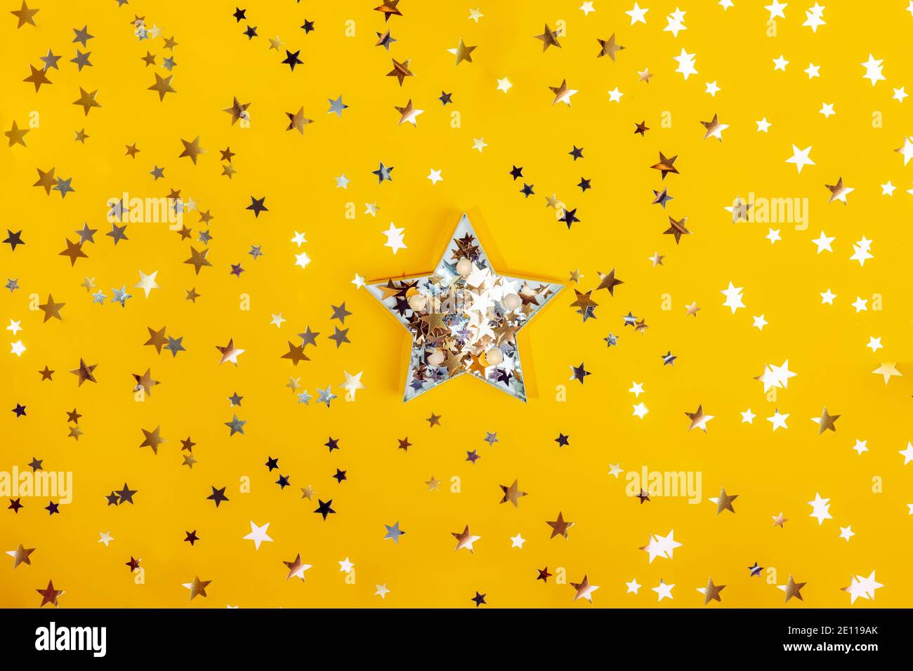 Forma a stella grande con stelle dorate e argentate scintillanti tra i confetti scintillanti a forma di stella sullo sfondo giallo. Concetto di festa. Essere unico, a. Foto Stock