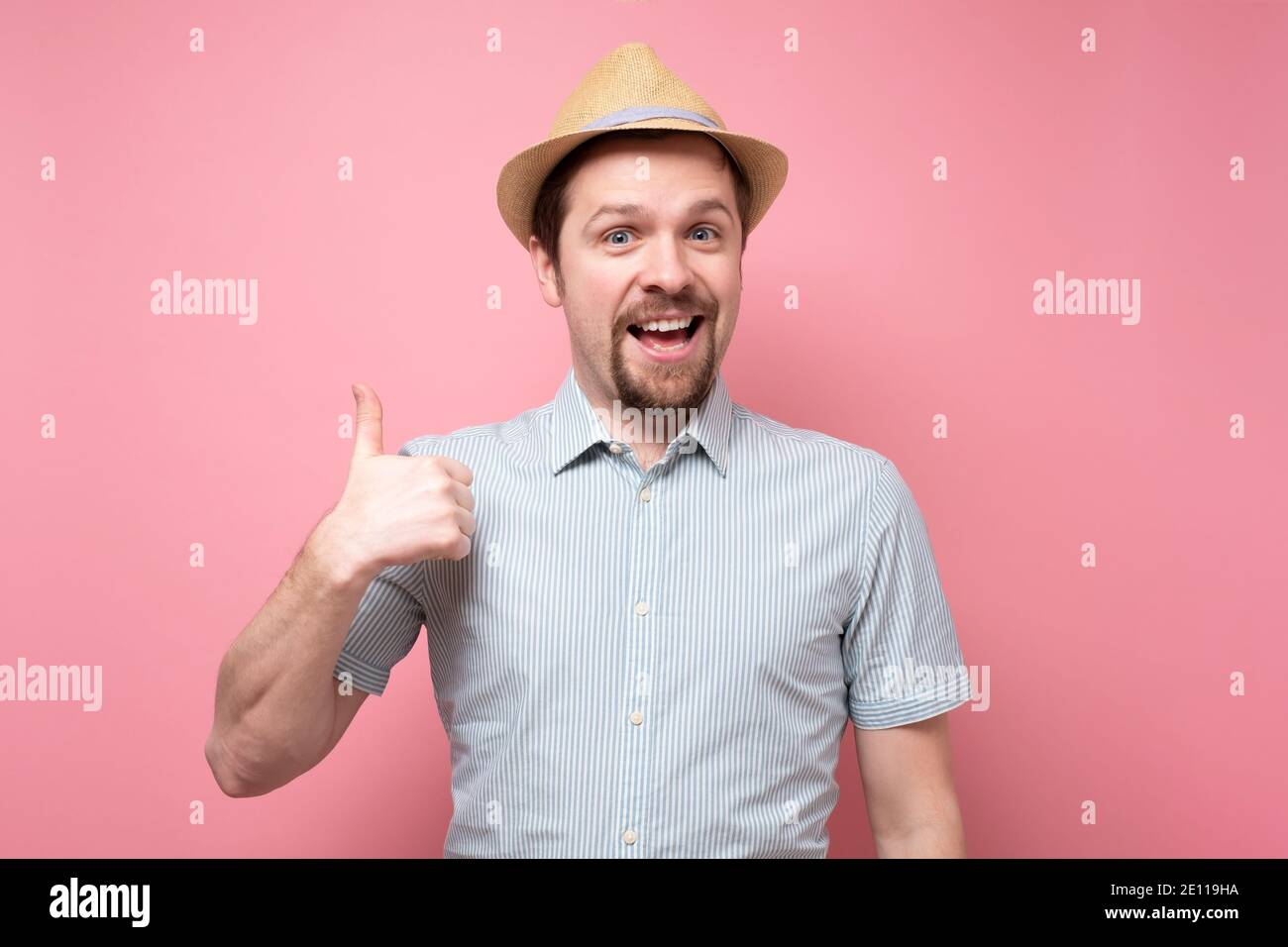 Attraente giovane uomo allegro in estate cappello mostrando pollici in su. Studio girato su parete gialla. Foto Stock