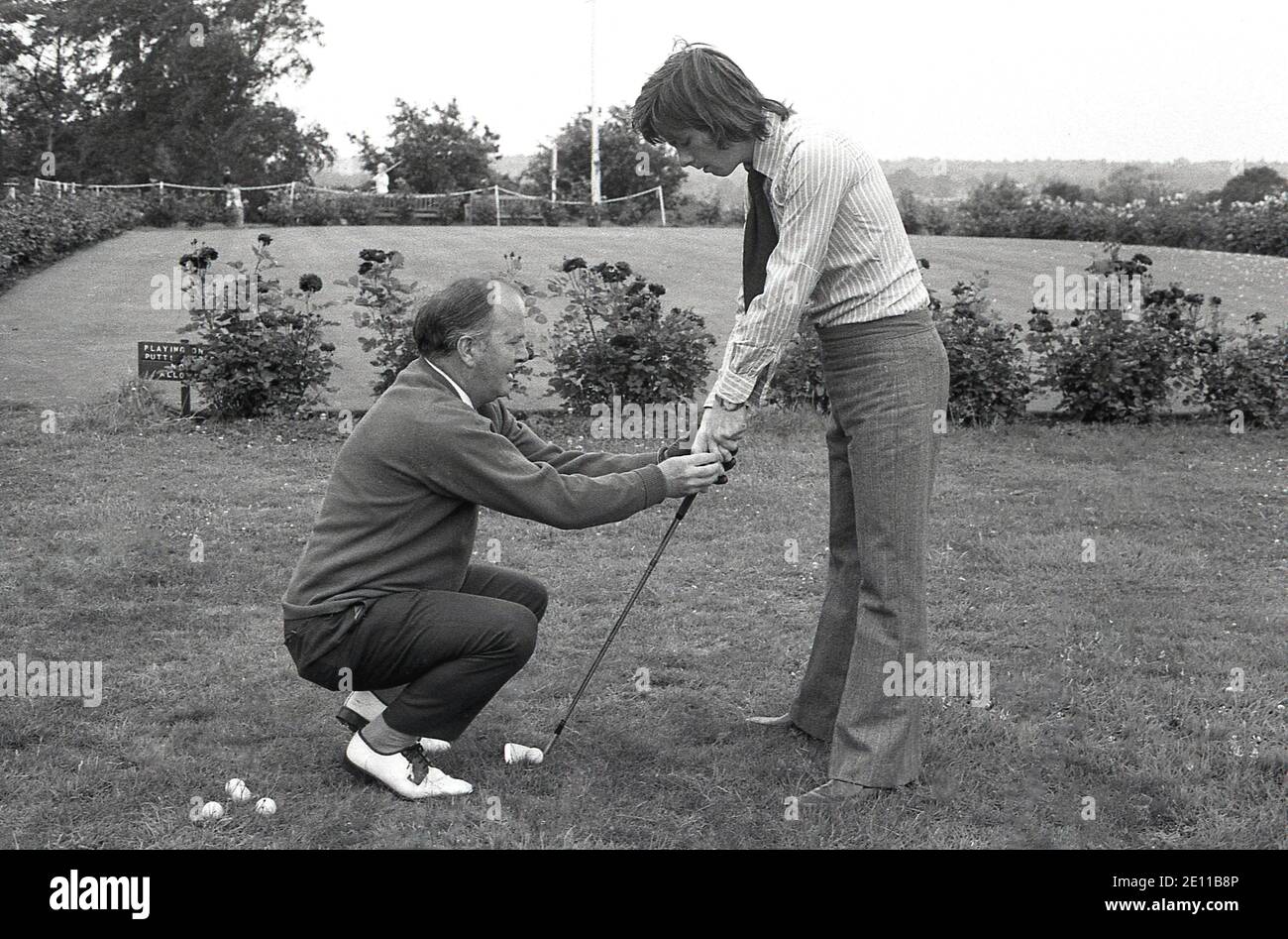 Anni '70, storico, fuori su una verga di erba da un putting green, un  professionista maschile senior di golf mostrando un giovane dilettante  maschile golfer, che sta tenendo il club di golf,