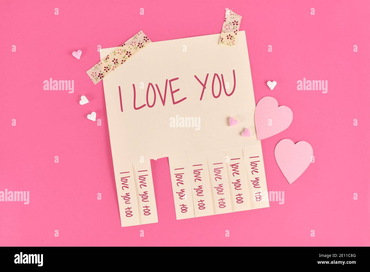 Giorno di San Valentino strappare la nota stub con il testo 'Io amo Tu' e rispondi 'anche io ti amo' su sfondo rosa con carta e cuori di zucchero Foto Stock