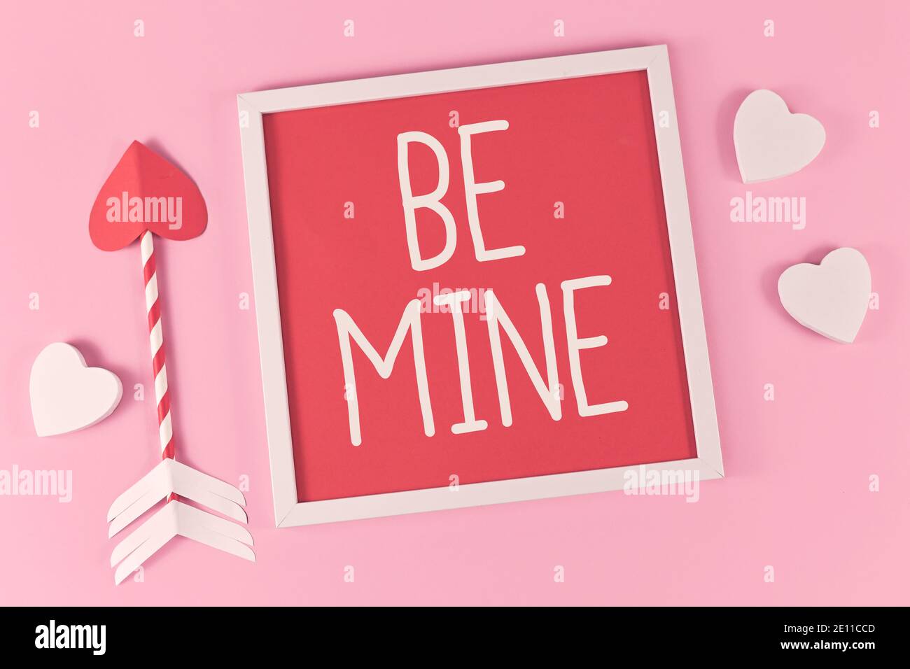 Composizione di San Valentino con cornice con testo 'be Mine', frecce d'amore cupide e cuori bianchi su sfondo rosa Foto Stock